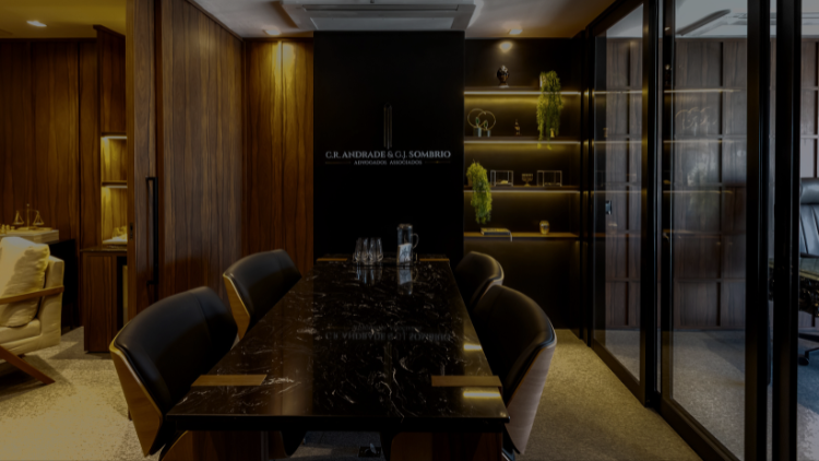 Sala de reuniões do escritório CR. Andrade & G.J. Sombrio, com mesa de mármore preto, cadeiras estofadas e logo institucional na parede.