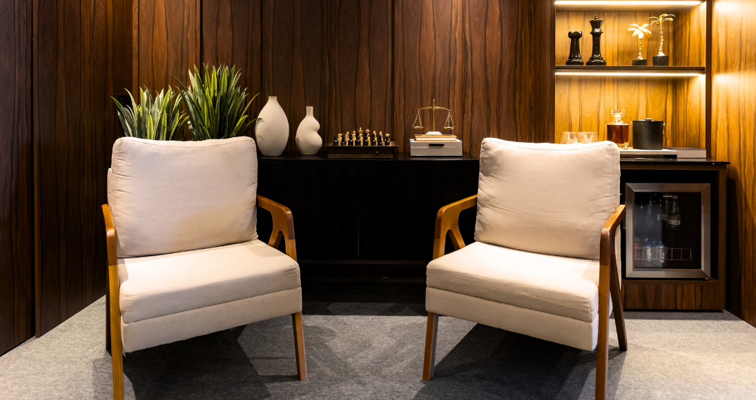 Área de espera do escritório CR. Andrade & G.J. Sombrio, com duas poltronas confortáveis, decoração com plantas, peças artísticas e frigobar embutido.